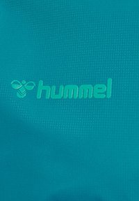 Teal sportstof met een textuurpatroon. Bevat een licht teal "hummel"-logo en bijenembleem, beide in het materiaal geperst.