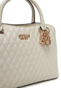 Borsa a mano in crema trapuntata con finitura lucida, dotata di hardware dorato, dettaglio del logo e un charm con due lettere. Manici doppi per il trasporto.