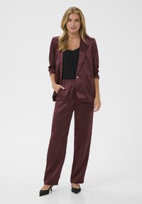 Conjunto de traje de satén burdeos que incluye un blazer ajustado con un solo botón, pantalones a juego y una blusa de encaje negra. Diseño slim-fit con bolsillos.
