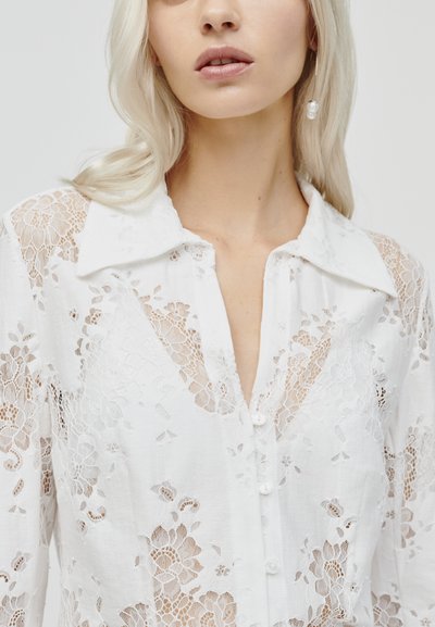 Witte kantblouse met bloemendessins, een kraag, een knoopsluiting aan de voorkant en een doorschijnende textuur met fijne details op de mouwen en borst.
