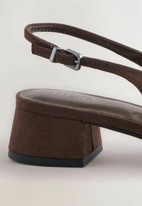 Ruda od suede slingback sandalai su kvadratiniu kulnu, reguliuojama juosta su metaliniu sagtimi ir lygaus odos pado.