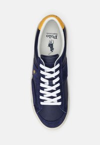Navy blue sneaker with leather and suede materials, white laces, yellow textured accents on the top, and a patterned insole with logo.
