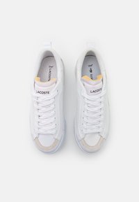Białe sneakersy z płóciennym wierzchem, minimalistyczny design i jasnobeżowe akcenty. Posiadają okrągły czubek, sznurowane zapięcie oraz wyściółkę kołnierza.