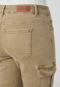 Khaki cargo kalhoty s hladkým povrchem, mají štítek v pase, dvě zadní kapsy a jednu boční kapsu.