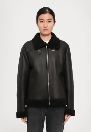 Mustmust nahkjakker shearling-krae, lukuga ees, kaks külge taskut ja tekstureeritud varrukad. Struktureeritud disain, mis on veidi lõdvem.