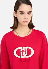 Felpa rossa con maniche lunghe, caratterizzata da un grande logo bianco impreziosito da strass. Tessuto morbido e design con scollo rotondo.