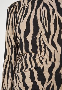 T-shirt à manches longues avec un motif de rayures de tigre beige et noir, en tissu texturé et avec des détails froncés sur les côtés.