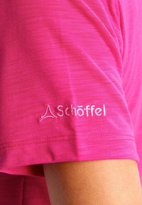 Chemise rose à manches courtes en tissu doux, présentant une texture subtile et un logo blanc brodé sur la manche.