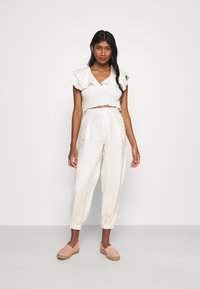 Top cropped branco com pregas e mangas rufadas, combinado com calças largas de linho bege claro e espadrilles rosa suave.