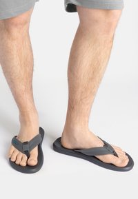 Graue Flip-Flops mit dicker Sohle und Stoffriemen. Mit einem kontrastierenden dunklen Riemen und einem blauen Akzent. Offenes Design für die Zehen, leichtes Material.