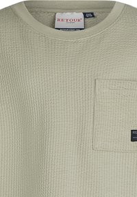 Jasnozielona koszulka w splot wafel, z okrągłym dekoltem, krótkimi rękawami oraz kieszonką na łatkę. Posiada małą naszywkę z logotypem marki na kieszeni.