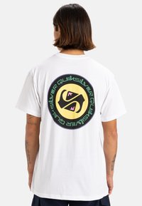 Camiseta de algodón blanca con un gran gráfico circular en la parte posterior, con un fondo amarillo, acentos en negro y rosa, y texto "Quiksilver".