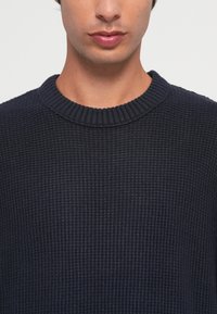 Pull en tricot bleu marine avec un col rond côtelé et un motif texturé, fabriqué à partir d'un tissu doux avec une finition lisse.