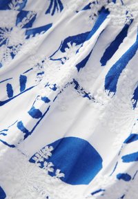 Biała tkanina z niebieskimi wzorami kwiatowymi i teksturowanym haftem. Zawiera szczegółowe ściegi i kontrastowe kolory dla zwiększenia wizualnego zainteresowania.