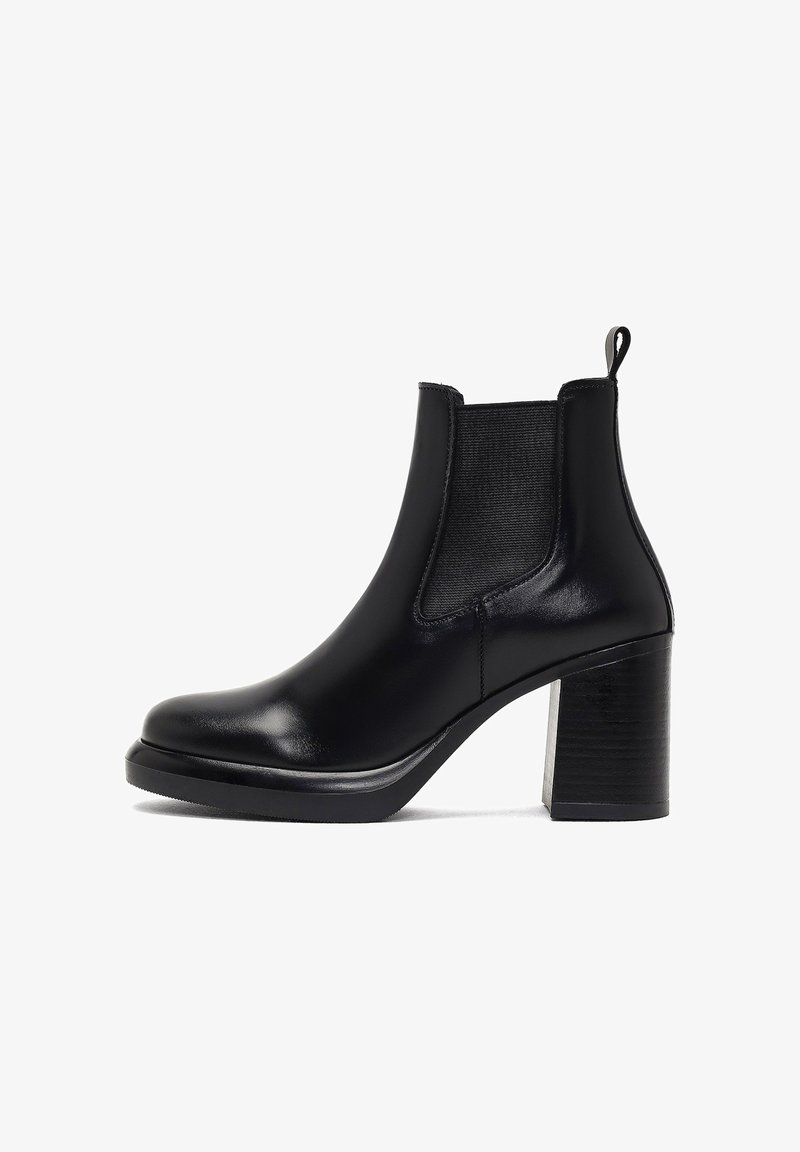 Bottine en cuir noir avec un talon bloc, des panneaux latéraux élastiques et une texture lisse. Le design est épuré, sans qu'aucune quincaillerie soit visible.