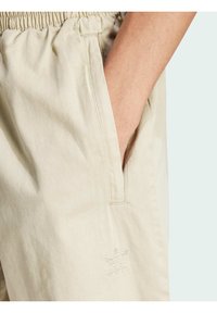 Pantaloni corti in cotone beige con elastico in vita, tasche laterali e un discreto logo Adidas ricamato in bianco nella parte bassa anteriore.