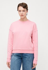 Felpa rosa con maniche lunghe, caratterizzata da accenti a forma di cuore argentati sulle maniche. Materiale morbido con una vestibilità comoda e polsini a costine.