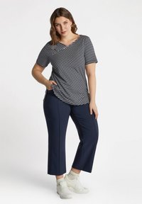 Camiseta de rayas en azul marino con un escote ligeramente asimétrico, combinada con pantalones recortados en azul marino y zapatillas blancas con suelas texturizadas.