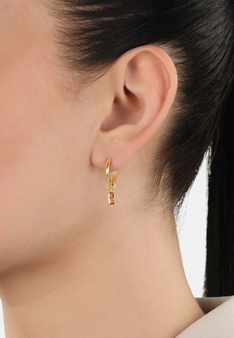 Orecchino a cerchio in oro con un ciondolo rettangolare appeso sotto. Il ciondolo presenta una pietra trasparente di colore ambra. Design semplice ed elegante.