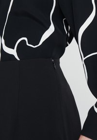 Svart klänning med ett vitt abstrakt mönster, med långa ärmar, en figurnära passform och en sidodragkedja för enkel påklädning.