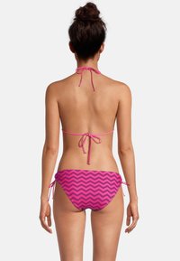 Bikini deux pièces rose avec un motif en zigzag. Col halter et nouages dans le dos, liens ajustables sur les côtés du bas. Texture de tissu lisse.