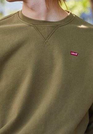 Oliwkowo zielona bluza z okrągłym dekoltem, wykonana z fakturowanej tkaniny, z małym czerwonym logo Levi's na piersi. Posiada widoczne detale przeszyć.