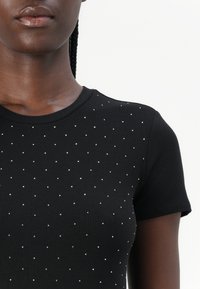 Black ribbed t-shirt featuring a slim fit, round neckline, and scattered silver studs for detail. Short sleeves complete the design.