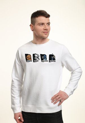 Hombre con sudadera blanca con cuatro cascos estilizados de Star Wars etiquetados como Armorer, Mando, Paz Vizsla y Bo-Katan en el pecho.