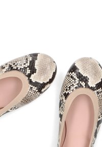 Paire de ballerines pour femmes avec motif peau de serpent beige et noir et semelles intérieures roses douces sur fond blanc.