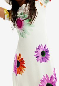 Abito bianco a coste con grandi motivi floreali dai colori vivaci in tonalità di viola, arancione, rosa e verde. Maniche corte con dettagli floreali.