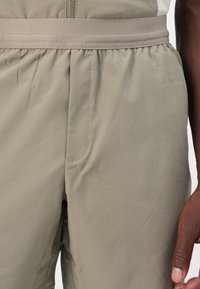 Shorts beiges en tissu léger avec une taille élastique, dotés d'une poche latérale et d'une texture lisse.