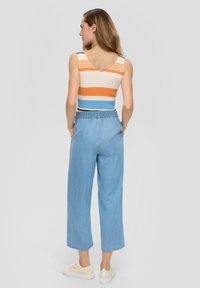 Gestreifter, gerippter Tanktop in den Farben Orange, Creme und Blau, kombiniert mit hellblauen weiten Hosen. Das Outfit wird mit beigen Sneakers abgerundet.