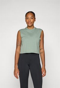 Light green cropped sleeveless top with a round neckline and logo detail, paired with black fitted leggings, showcasing smooth fabric texture.