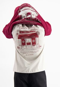 T-shirt met een lichtgrijze basis, met een maroon bloemenwinkel grafisch ontwerp op de achterkant. Korte mouwen en een ontspannen pasvorm.