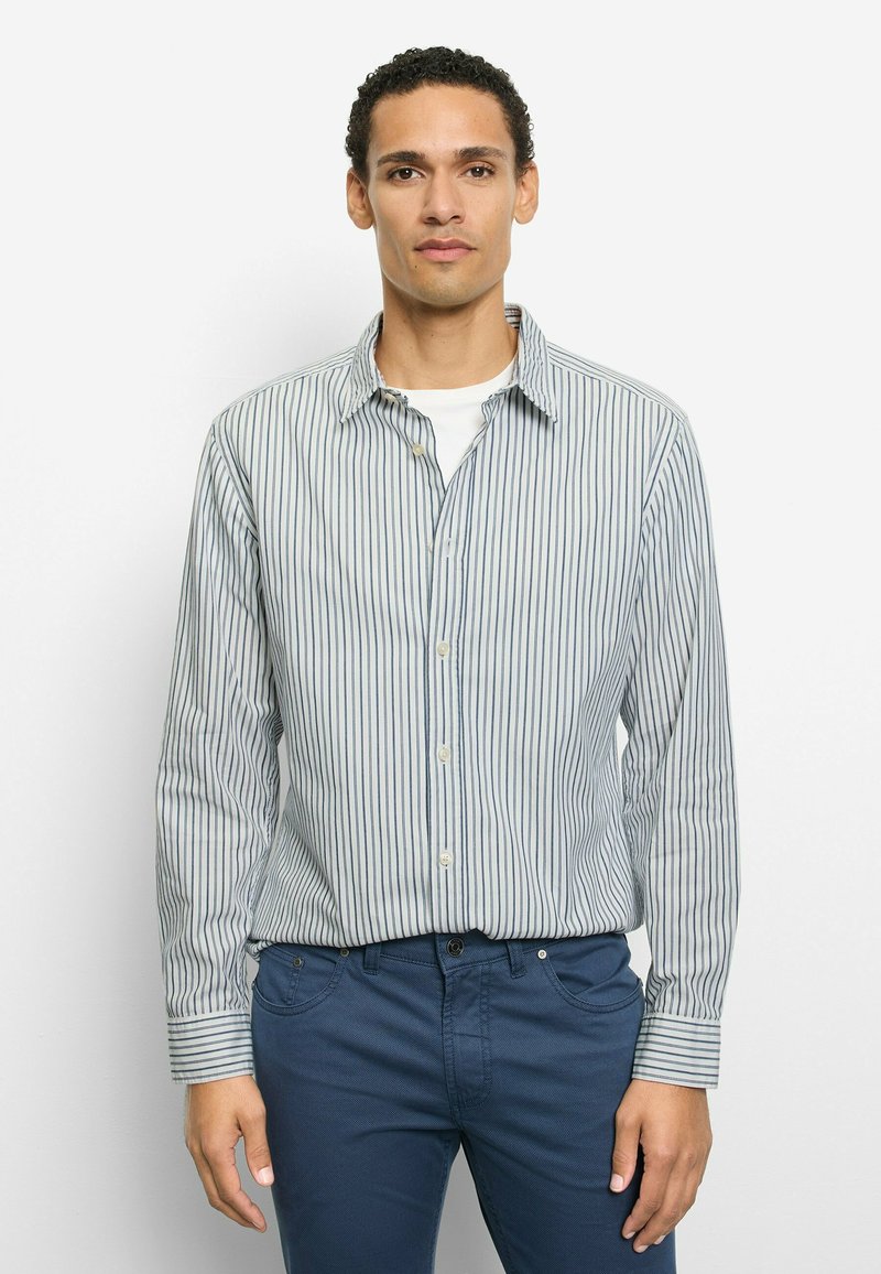 Gestreiftes Hemd mit Knöpfen in hellblauem und weißem Stoff, mit klassischem Kragen, langen Ärmeln und entspanntem Schnitt. Kombiniert mit blauen Hosen.