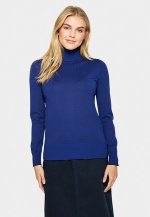 Blauwe coltrui gemaakt van ribbelbreisel, met lange mouwen en een getailleerd ontwerp, gecombineerd met een donkere rok.