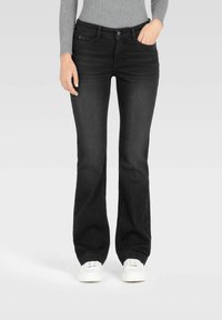 Sorte flared jeans laget av denim, med midjehøyde, frontlommer og en jevn tekstur, sammen med hvite sneakers.