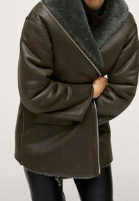 Bruin leren jas met een brede, zachte, grijze kraag, voorzien van een diagonale rits. Het ontwerp heeft een ontspannen pasvorm en een gestructureerde afwerking.