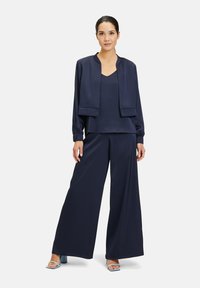 Ensemble deux pièces en satin bleu marine comprenant une veste courte à manches longues et un pantalon à jambes larges. Texture lisse, design minimaliste et accents élégants.