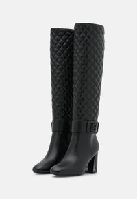 Par de botas negras altas hasta la rodilla con ejes acolchados, parte de cuero suave en el pie, tacones de bloque y correas decorativas con hebillas alrededor de los tobillos.