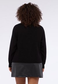 Maglione nero lavorato a maglia con vestibilità ampia e maniche lunghe, abbinato a una gonna corta in pelle nera lucida con accenti metallici.