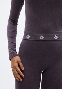 Μπλούζα με μακριά μανίκια, εφαρμοστή, και αντίστοιχο κολάν σε σκούρο μοβ ύφασμα. Η μέση έχει διακοσμητική λεπτομέρεια με ανοιχτό γκρι λουλουδάτα μοτίβα.