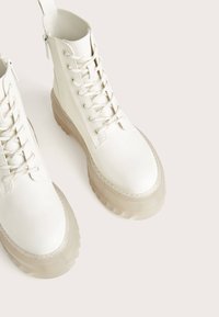 Vita snörkängor i läder har en slät lävoverdel och en genomskinlig texturerad sula med ett robust mönster.