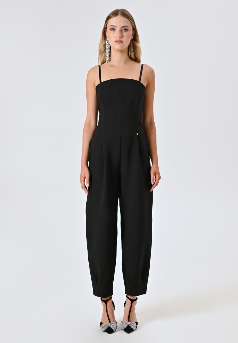 Schwarzer Jumpsuit mit einem quadratischen Ausschnitt, dünnen Trägern und schmal zulaufenden Beinen, aus glattem Stoff mit einem minimalen silbernen Akzentdetail.