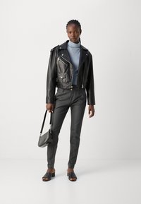Zwarte leren cropped bikerjack met zilveren ritsen, gecombineerd met een lichtblauw turtleneck, op maat gemaakte zwarte broek en zwarte instapsandalen.