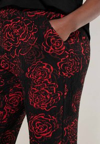 Zwarte broek met een textuurstof en een rood bloemenpatroon, inclusief grote rozenontwerpen en zijzakken.