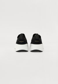 Chaussures de sport noires avec une tige en mesh texturé, une semelle intermédiaire blanche et une semelle extérieure noire. Logo "TWINESET" en or à l'arrière.