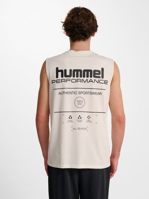 Man met krullend haar die van achteren te zien is, draagt een mouwloos beige topje met de tekst en logo's "hummel PERFORMANCE AUTHENTIC SPORTSWEAR" op de rug.