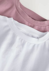 Zwei Baumwoll-T-Shirts in Hellrosa und Weiß. Das weiße Shirt hat ein strukturiertes, gerafftes Detail am Kragen.