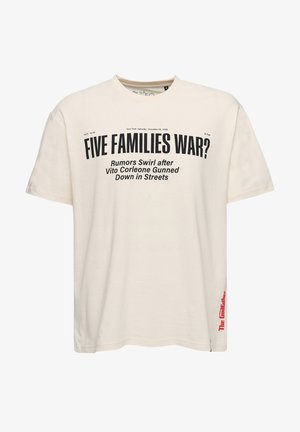 Beżowa bawełniana koszulka z czarnym napisem, okrągłym dekoltem i krótkimi rękawami. W połączeniu z jasnoniebieskimi dżinsami i białymi trampkami.